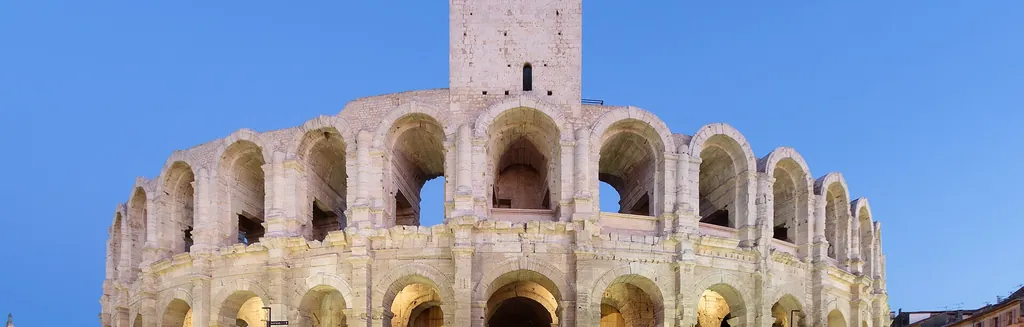 Les arènes romaines d'Arles illuminées à l'heure bleue, avec en arrière-plan la lumière dorée de la Provence et, plus loin, les grands espaces de la Camargue
